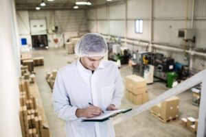 Man with a hairnet writing on a clipboard standing about a distribution center